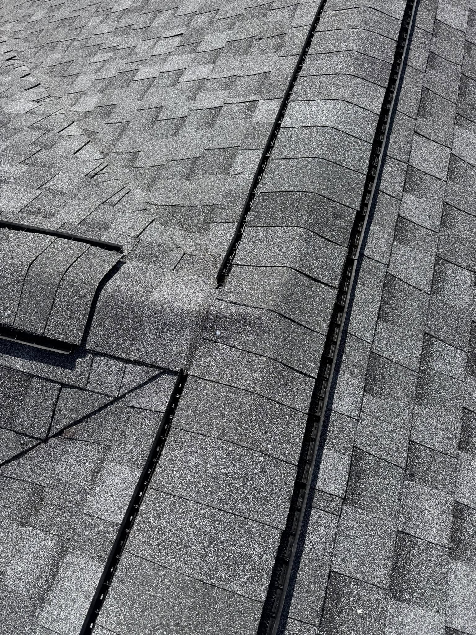 Close-up aerial view of gray asphalt shingles with metal roof flashing and gutters, showing roofing material detail and installation