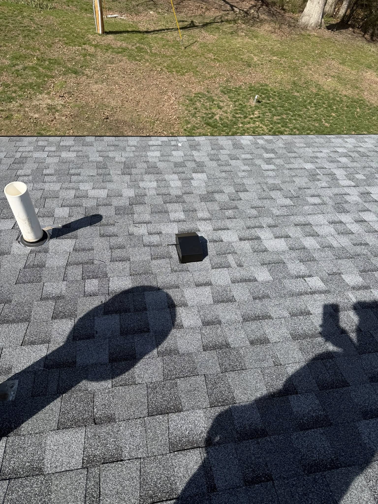 Newly installed asphalt shingle roof with gray dimensional shingles and white PVC pipe penetration