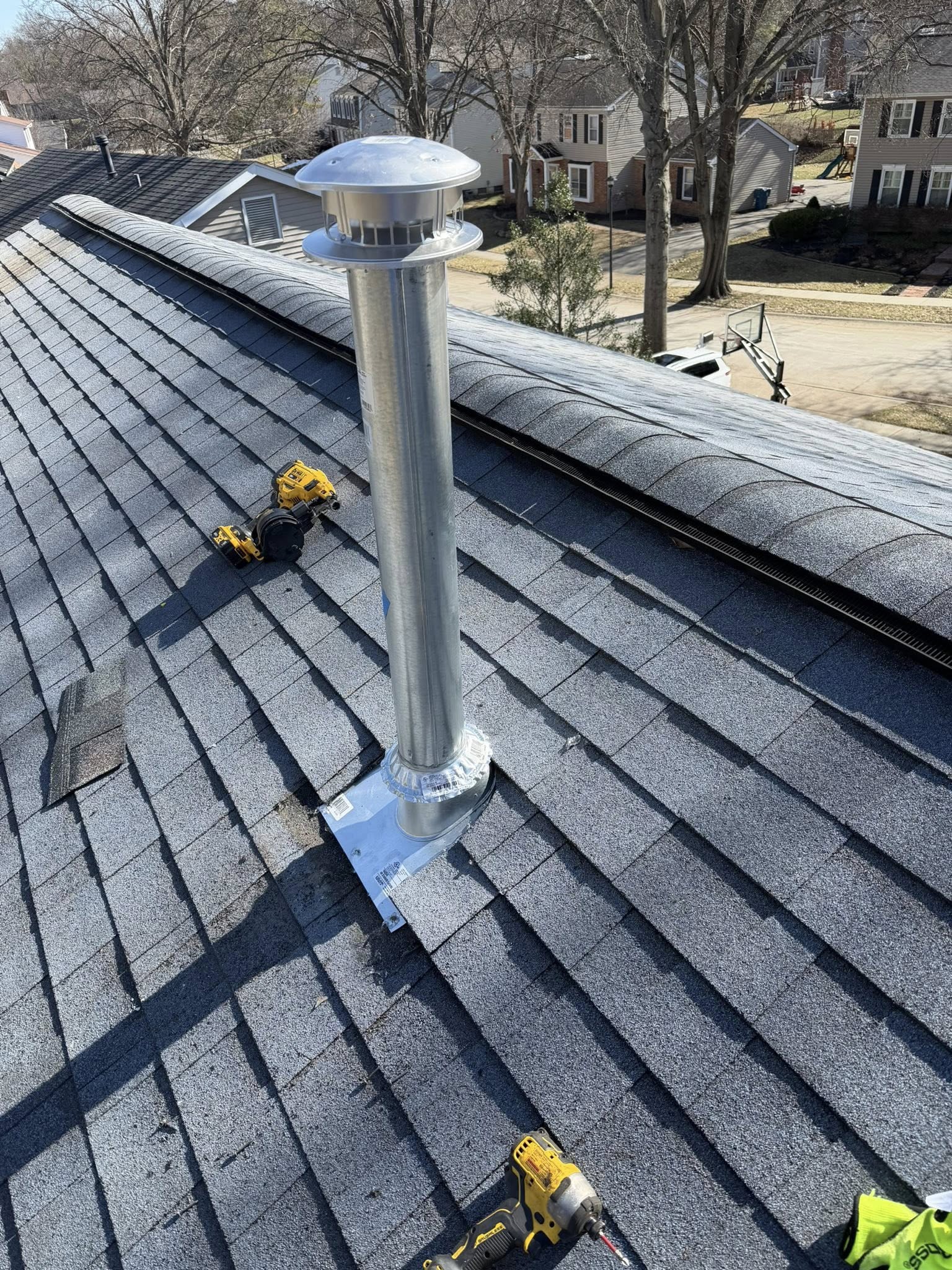 Roofer installing new chimney flashing on residential asphalt shingle roof with tools visible