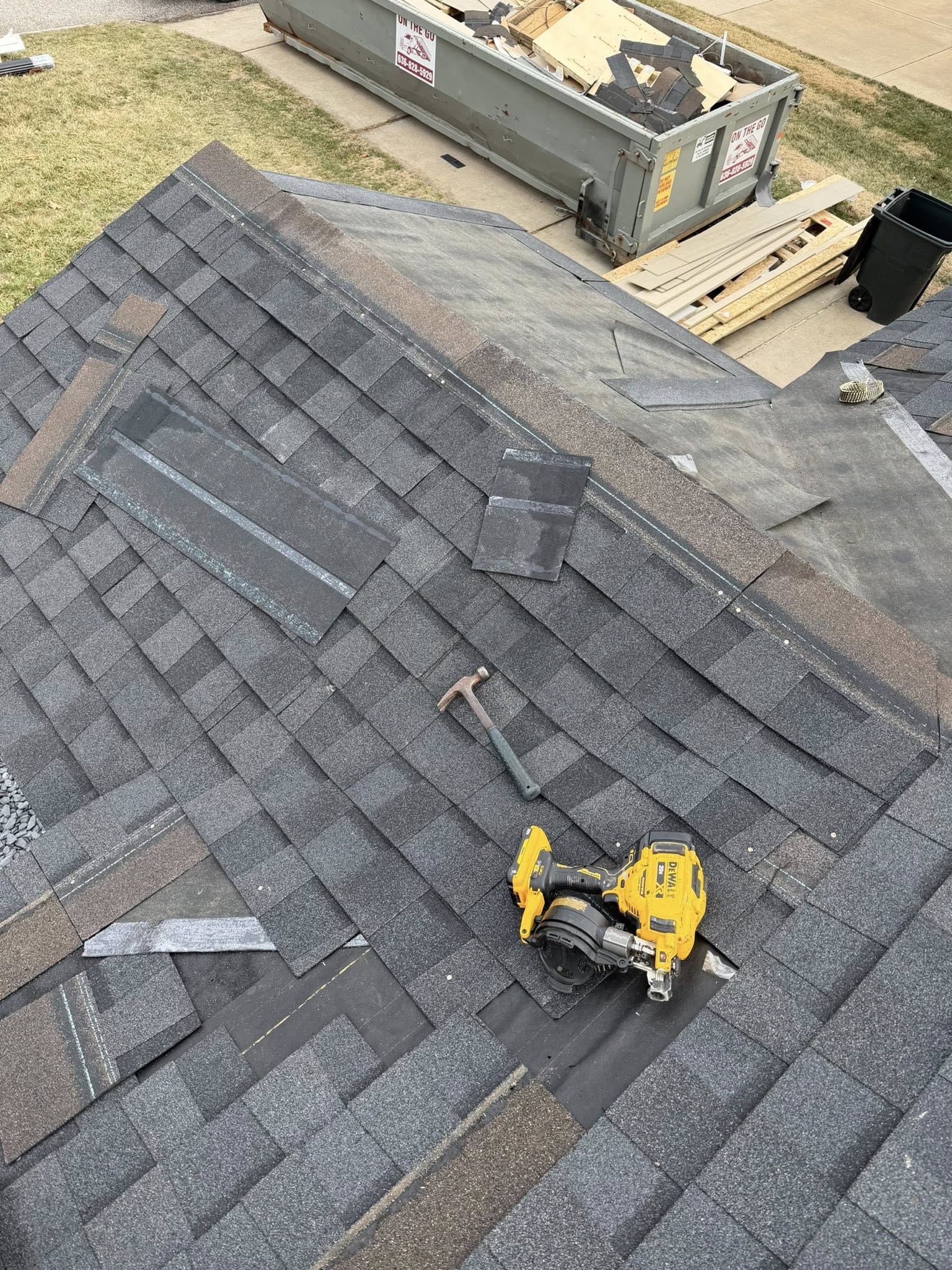 Roofer using pneumatic nail gun to install asphalt shingles during active roof replacement project