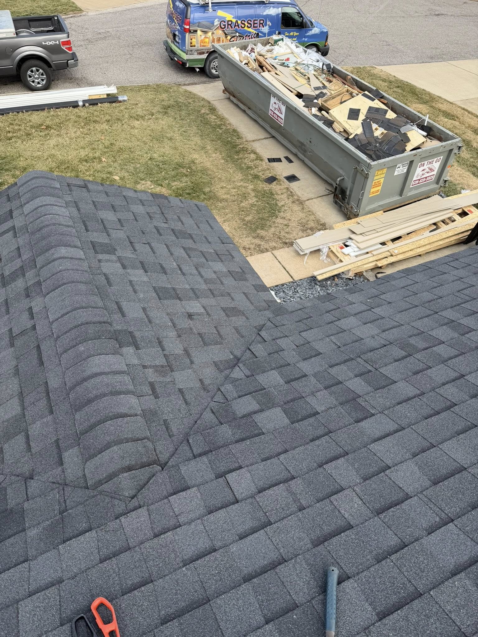 Roofer installing dark asphalt shingles on residential roof during active roof replacement project