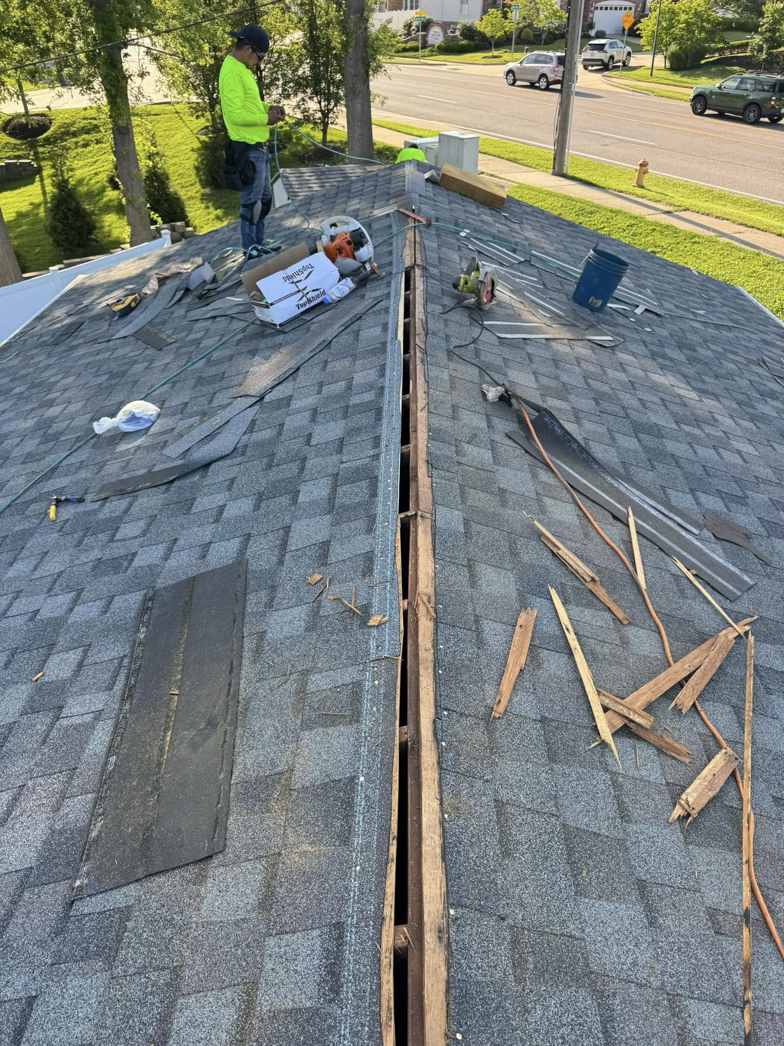 Roofing crew actively installing new shingles on residential roof with ridge vent and removal of old materials