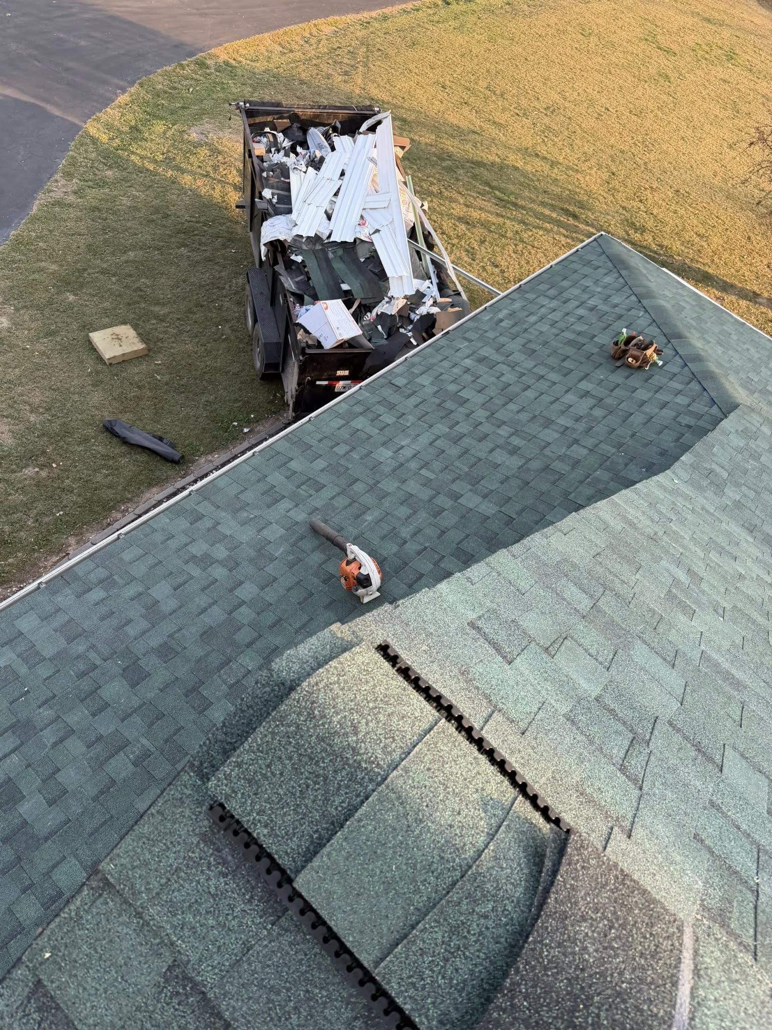 Aerial view of roofers installing new shingles on residential roof with debris removal truck on lawn