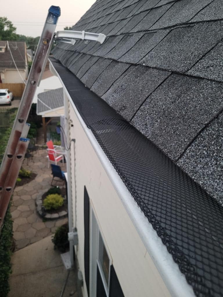 Residential roof repair in progress showing asphalt shingles, gutters, and protective mesh netting installation
